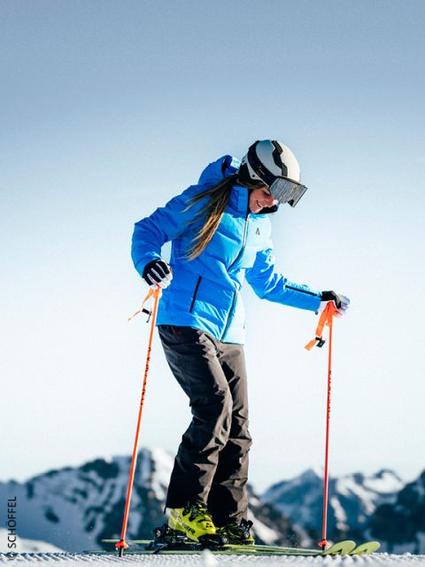 Persona con chaqueta azul y casco esquiando sobre nieve con montañas al fondo en un día claro y soleado.