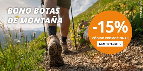Una mujer camina por una ladera rocosa con picos nevados al fondo. Un gran círculo naranja muestra "-15%" y un código promocional para un descuento en botas de montaña con el texto "BONO BOTAS DE MONTAÑA".