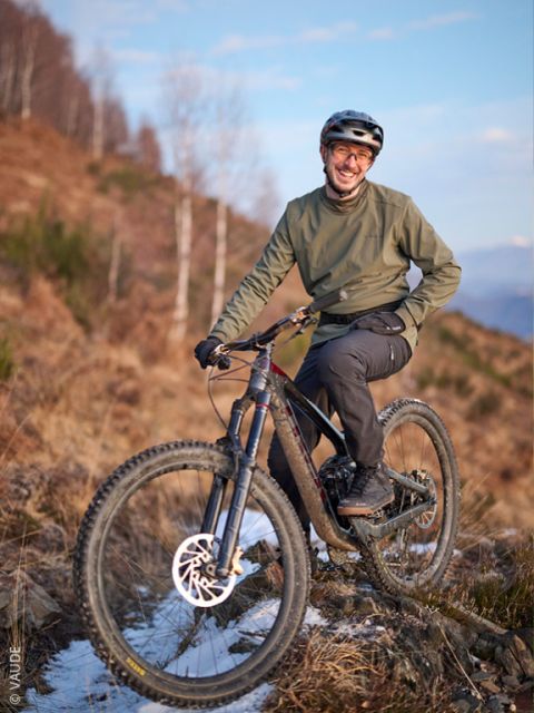 Una persona con casco y chaqueta verde sonríe mientras posa con una bicicleta de