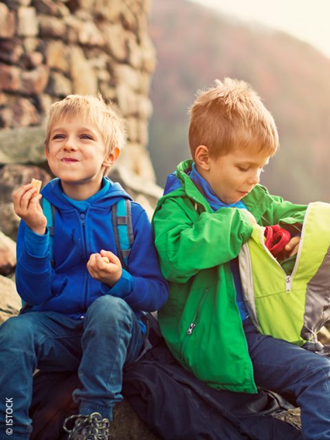 Dos niños pequeños están sentados afuera sobre rocas. Uno está comiendo un bocad