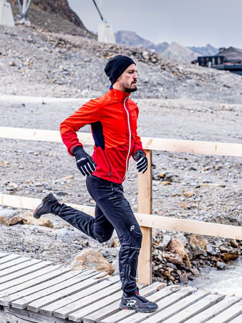 Un hombre con una chaqueta roja, pantalones negros, guantes y un gorro camina po